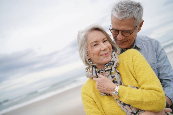 Portrait of attractive vibrant senior couple embracing on beach in fall                               - Foto, Imagem