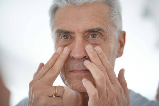   Hombre mayor guapo aplicando crema facial en el espejo
                              - Foto, imagen