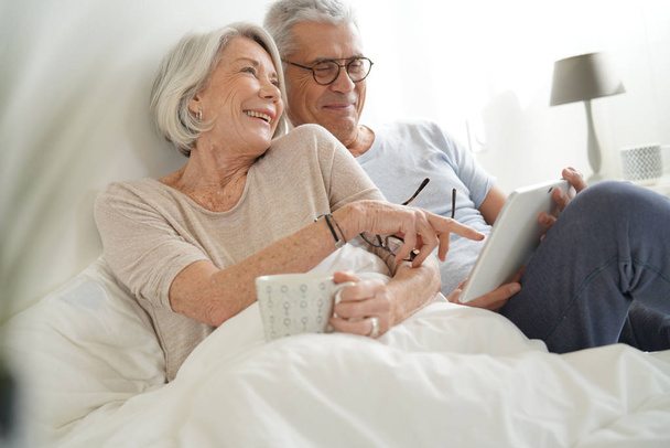   Senior couple relaxing in bed looking at tablet                              - Fotó, kép