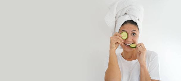 Vibrant brunette with towel turban and cucumber on eye on white background - Zdjęcie, obraz