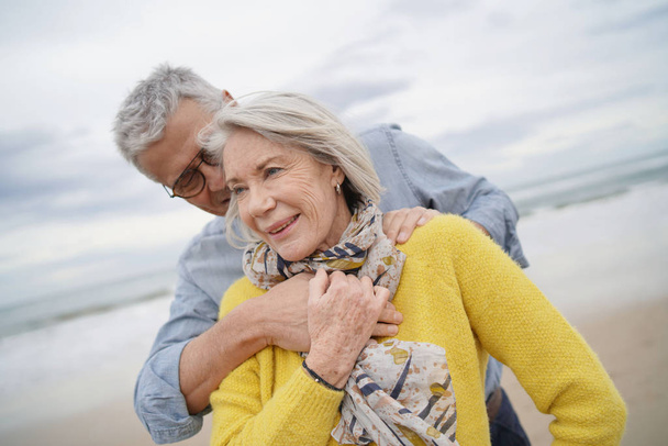 Ritratto di attraente vibrante coppia di anziani che si abbraccia sulla spiaggia in autunno
                               - Foto, immagini