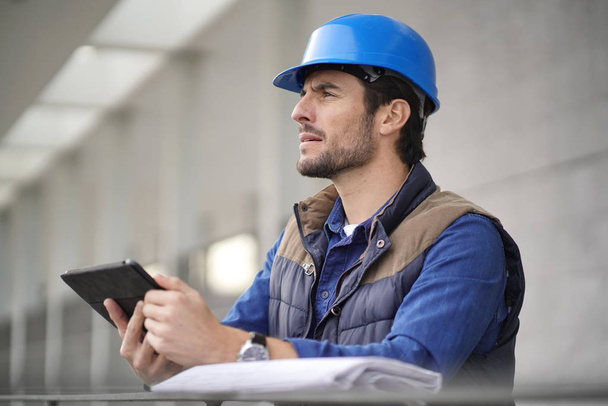 Handsome building expert in hardhat outdoors with tablet and blueprint - Fotó, kép