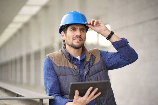 Especialista em construção atraente em hardhat verificando a visão com tablet
 - Foto, Imagem
