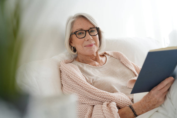 Beautiful senior woman relaxing in bed reading                               - Photo, image