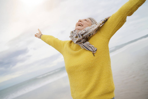  Carefree energetic senior woman playing around on beach in fall                              - Zdjęcie, obraz