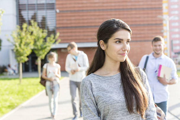 Усміхнена дівчина-підліток дивиться далеко під час прогулянки з друзями в університетському містечку
 - Фото, зображення