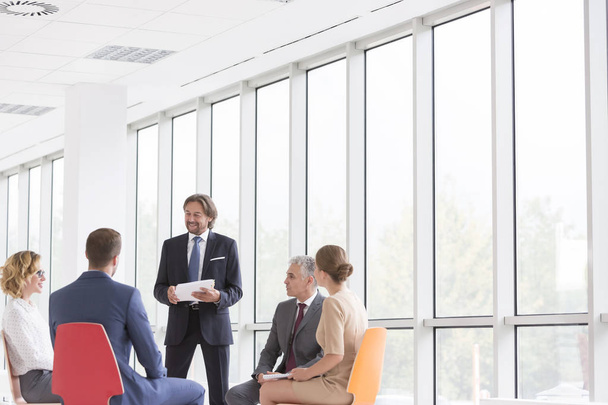 Empresario discutiendo con colegas contra ventana en nueva oficina
 - Foto, Imagen