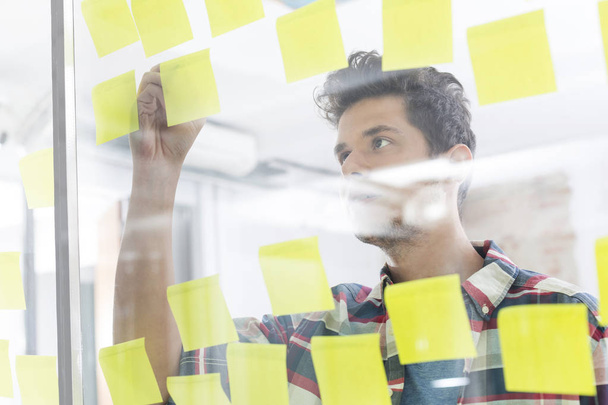 Young businessman writing on sticky notes in office - Foto, Imagem