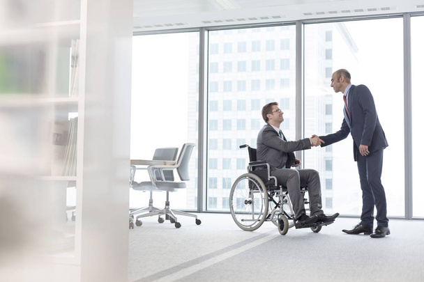 Businessman shaking hands with smiling disabled colleague in boardroom at office - Foto, immagini
