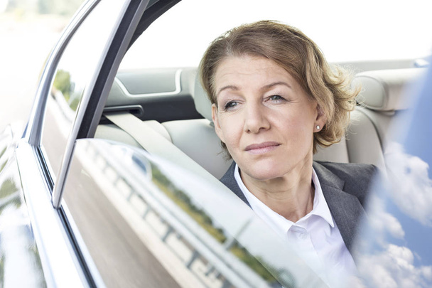 Thoughtful businesswoman looking through window while sitting in car - Fotografie, Obrázek