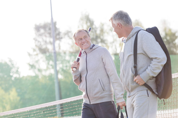 Smiling men in sports clothing talking while walking on tennis court - Foto, Imagen