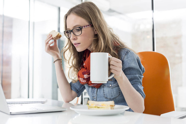 Businesswoman using laptop computer while having breakfast in office - Φωτογραφία, εικόνα