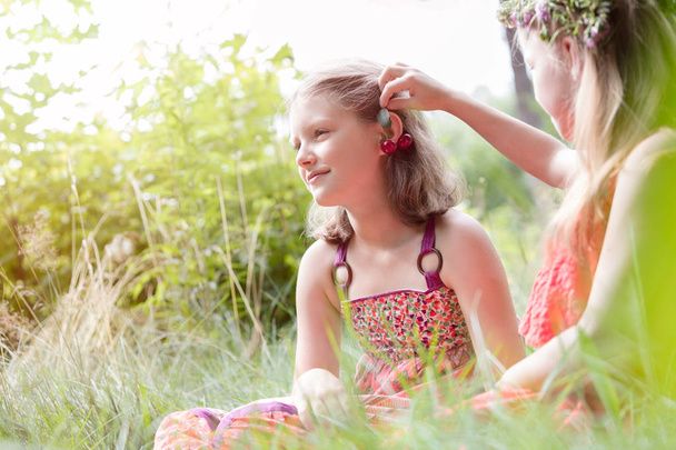 Menina bonito segurando folha na orelha do amigo no parque
 - Foto, Imagem