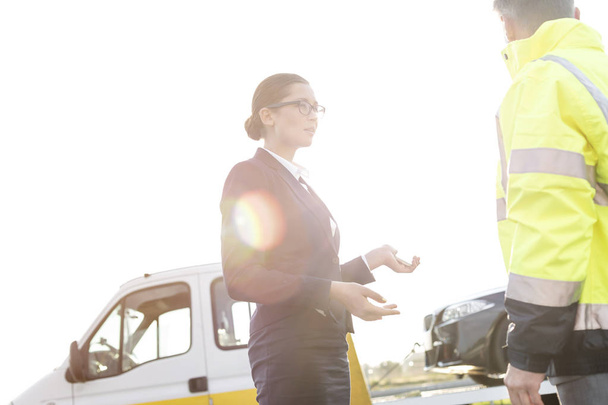 Businesswoman talking to tow truck driver against sky - Foto, Imagen