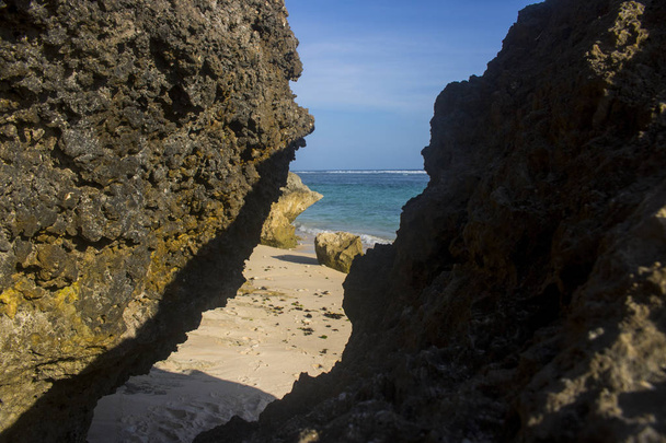 Sonne beleuchtete Felsen am Sandstrand mit Meer und blauem Himmel - Foto, Bild