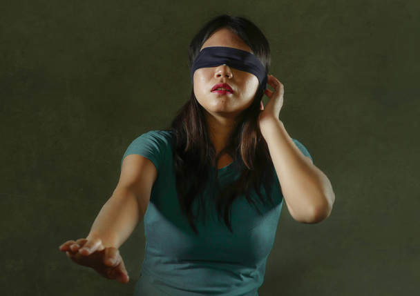 young scared and blindfolded Asian Korean teenager girl lost and confused playing dangerous internet viral challenge isolated on dark background under edgy and dramatic studio light - Foto, Imagen