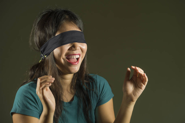 young happy and cute blindfolded Asian Korean teenager girl excited playing dangerous internet viral challenge isolated on dark background under edgy and dramatic studio light - Zdjęcie, obraz