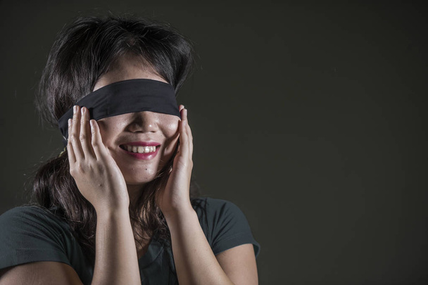 young happy and cute blindfolded Asian Korean teenager girl excited playing dangerous internet viral challenge isolated on dark background under edgy and dramatic studio light - Foto, Imagen