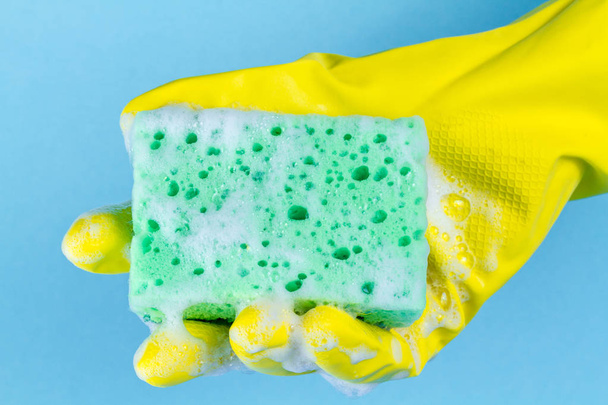 A hand in gloves with a foamy sponge for washing dishes on a blue background. Washing dishes, cleaning  - Fotoğraf, Görsel