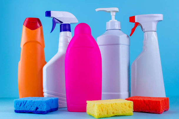 Various bottles, sprays for cleaning the house and colored sponges for washing dishes on a blue background. Cleaning concept - 写真・画像
