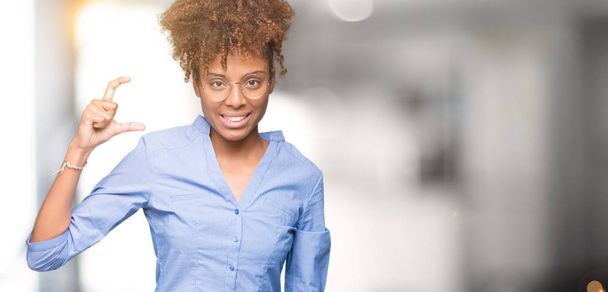Красивая молодая африканская деловая женщина на изолированном фоне улыбается и уверенно жестикулирует рукой, делая знак размера пальцами, глядя и камеру. Концепция измерения
. - Фото, изображение