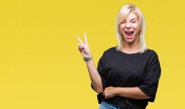 Young beautiful blonde woman over isolated background smiling with happy face winking at the camera doing victory sign. Number two. - Fotografie, Obrázek