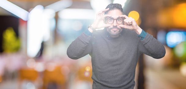 Young handsome man wearing glasses over isolated background Trying to open eyes with fingers, sleepy and tired for morning fatigue - Foto, afbeelding