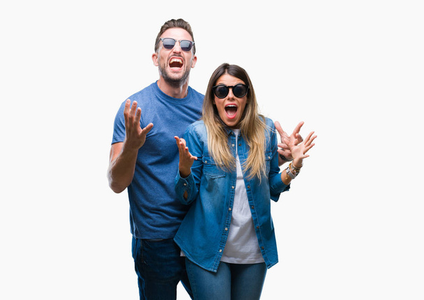 junges verliebtes Paar mit Sonnenbrille vor isoliertem Hintergrund, das verrückt und erfolgsverrückt mit erhobenen Armen und geschlossenen Augen aufgeregt feiert. Siegerkonzept - Foto, Bild