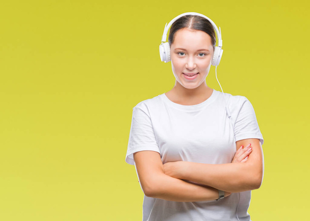 Молода біла жінка слухає музику в навушниках над ізольованим фоном щасливе обличчя, посміхаючись схрещеними руками, дивлячись на камеру. Позитивна особа
. - Фото, зображення