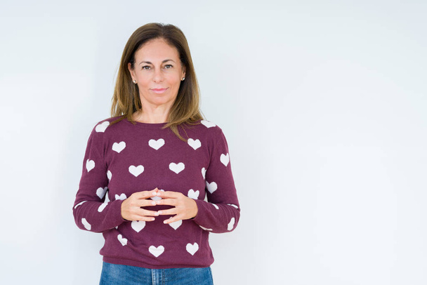 Beautiful middle age woman wearing heart sweater over isolated background Hands together and fingers crossed smiling relaxed and cheerful. Success and optimistic - Photo, Image