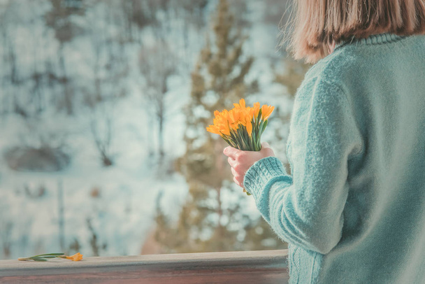 woman with a yellow bouquet of spring flowers in her hands on a snow day - Foto, afbeelding