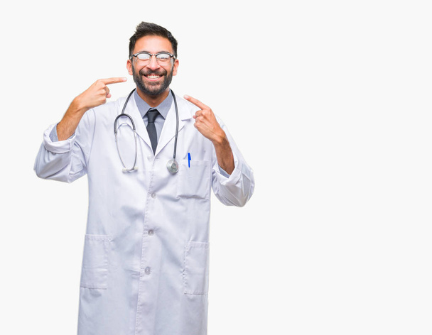 Adult hispanic doctor man over isolated background smiling confident showing and pointing with fingers teeth and mouth. Health concept. - Foto, immagini