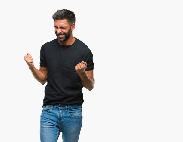Adult hispanic man over isolated background very happy and excited doing winner gesture with arms raised, smiling and screaming for success. Celebration concept. - Photo, Image