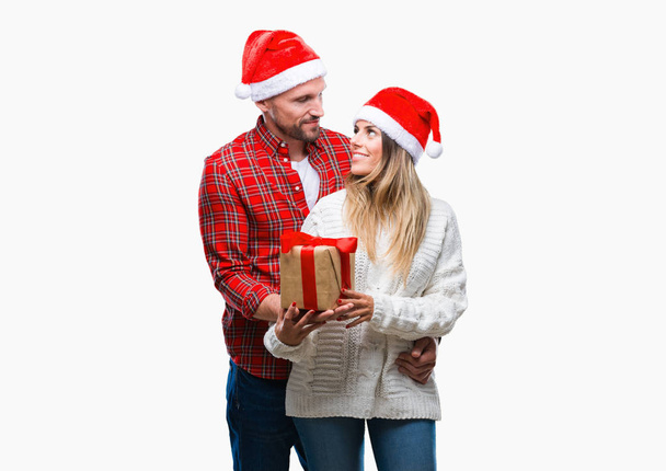 junges verliebtes Paar trägt Weihnachtsmütze und hält Geschenk über isoliertem Hintergrund mit einem selbstbewussten Gesichtsausdruck auf intelligentem Gesichtsdenken ernst - Foto, Bild