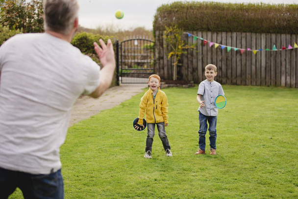 Rear view of a mid adult father throwing a tennis ball to his son and his friend. They are having fun and playing a game. - Photo, image