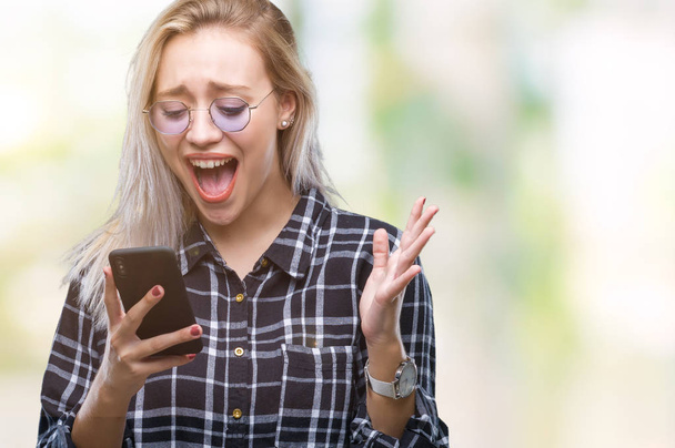 Młoda kobieta blonde tekstylny wysyłanie wiadomości przy użyciu smartfona na na białym tle bardzo szczęśliwy i podekscytowany, zwycięzca wyrażenie świętuje zwycięstwo krzyczy z uśmiechem i podniósł ręce - Zdjęcie, obraz