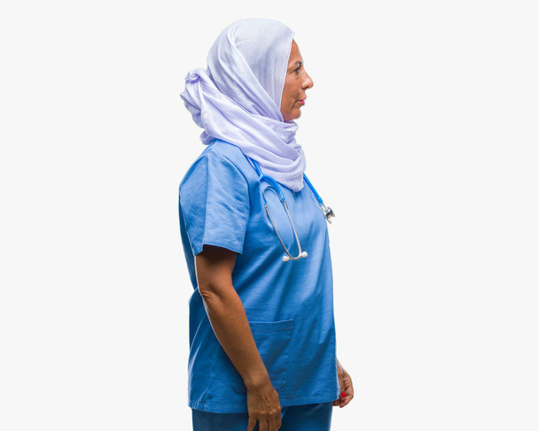 Enfermera árabe mayor de mediana edad que usa hijab sobre un fondo aislado mirando hacia un lado, pose de perfil relajado con cara natural con sonrisa confiada
. - Foto, imagen