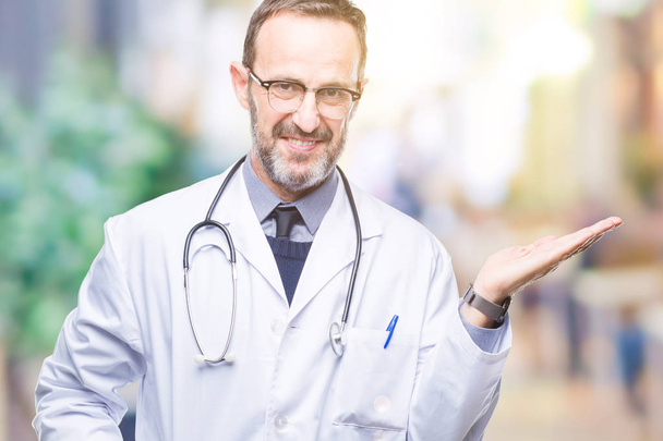 Middle age senior hoary doctor man wearing medical uniform isolated background smiling cheerful presenting and pointing with palm of hand looking at the camera. - Fotó, kép