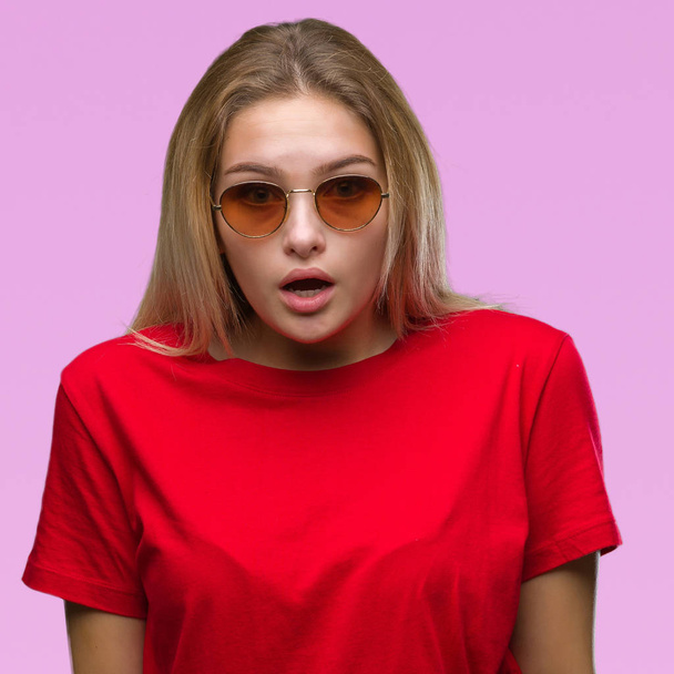Young caucasian woman wearing sunglasses over isolated background afraid and shocked with surprise expression, fear and excited face. - Photo, Image