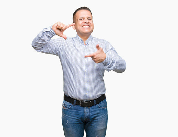 Арабський бізнесмен середнього віку над ізольованим тлом посміхається роблячи рамку руками і пальцями з щасливим обличчям. Концепція творчості та фотографії
. - Фото, зображення