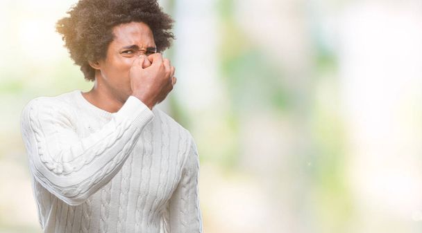 Afro american man over isolated background smelling something stinky and disgusting, intolerable smell, holding breath with fingers on nose. Bad smells concept. - Foto, imagen