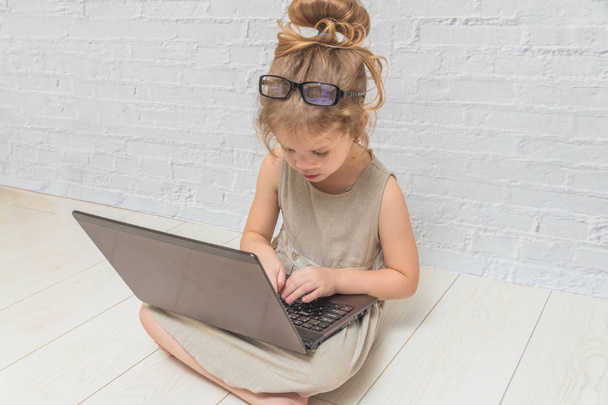 girl, child businesswoman working at a laptop, against a white brick wall - Фото, изображение