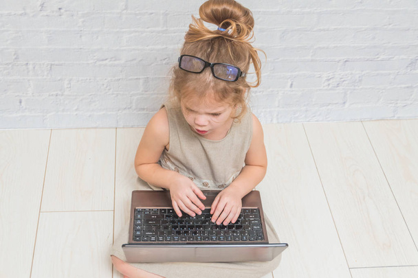 girl, child businesswoman working at a laptop, against a white brick wall - Zdjęcie, obraz
