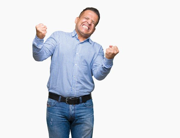 Hombre de negocios árabe de mediana edad sobre fondo aislado muy feliz y emocionado haciendo gesto ganador con los brazos levantados, sonriendo y gritando por el éxito. Concepto de celebración
. - Foto, Imagen