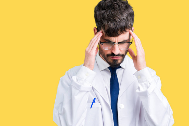 Young professional scientist man wearing white coat over isolated background with hand on head for pain in head because stress. Suffering migraine. - Фото, изображение
