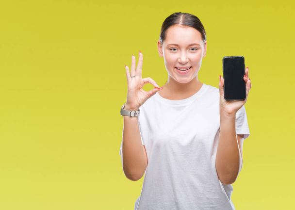 Mladá krásná žena Kavkazský zobrazeno smartphone obrazovky nad izolované pozadí dělá ok cedulka s prsty, vynikající symbol - Fotografie, Obrázek