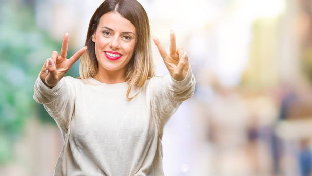Young beautiful woman casual white sweater over isolated background smiling looking to the camera showing fingers doing victory sign. Number two. - Photo, Image