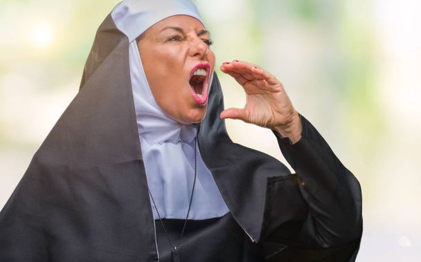 Középkorú idősebb keresztény katolikus apáca nő felett elszigetelt háttér kiabálás és sikoltozik hangosan oldalára állt a kéz a száj. Kommunikáció fogalma. - Fotó, kép
