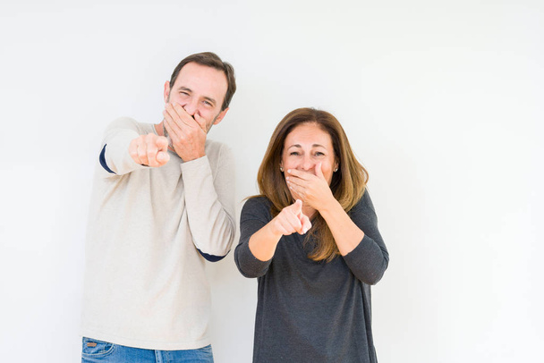 Beautiful middle age couple in love over isolated background Laughing of you, pointing to the camera with finger hand over mouth, shame expression - 写真・画像