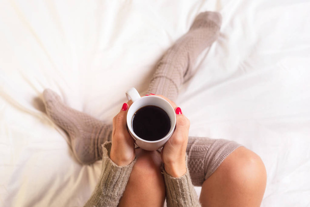 Γυναίκα κάθεται στο κρεβάτι, πίνοντας ένα φλιτζάνι του καφέ - Φωτογραφία, εικόνα